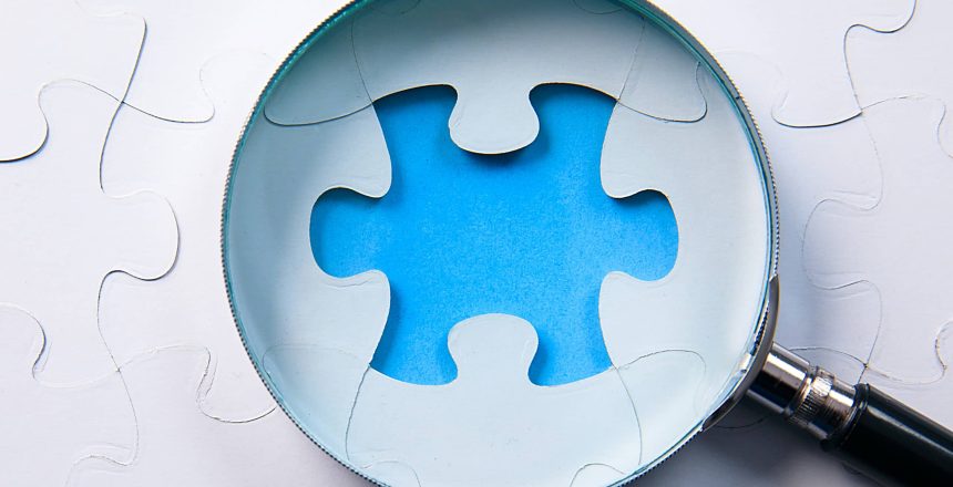 a missing blue puzzle piece under a magnifying glass representing the space for inpatient clinical medical coders at healthcare organizations